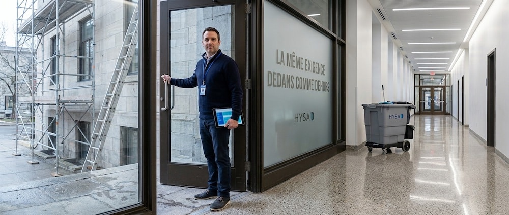 Gestionnaire municipal sur le seuil d’un édifice public québécois, entre la façade inspectée et le corridor entretenu, tablette en main